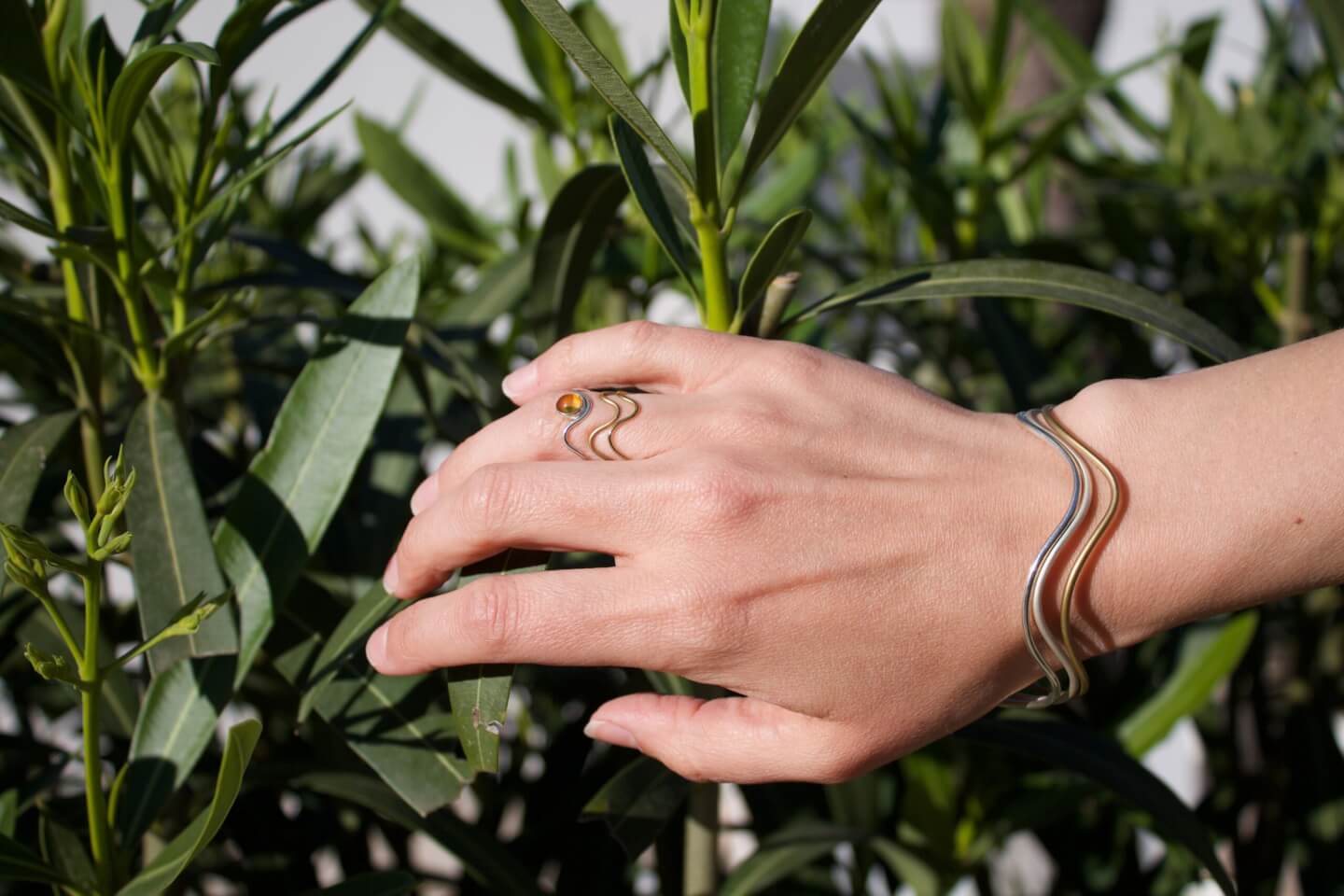 Nahaufnahme einer Hand mit wellenförmigen Schmuck aus Gold und Silber